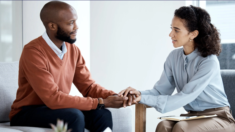 A man and a woman sit near each other holding hands