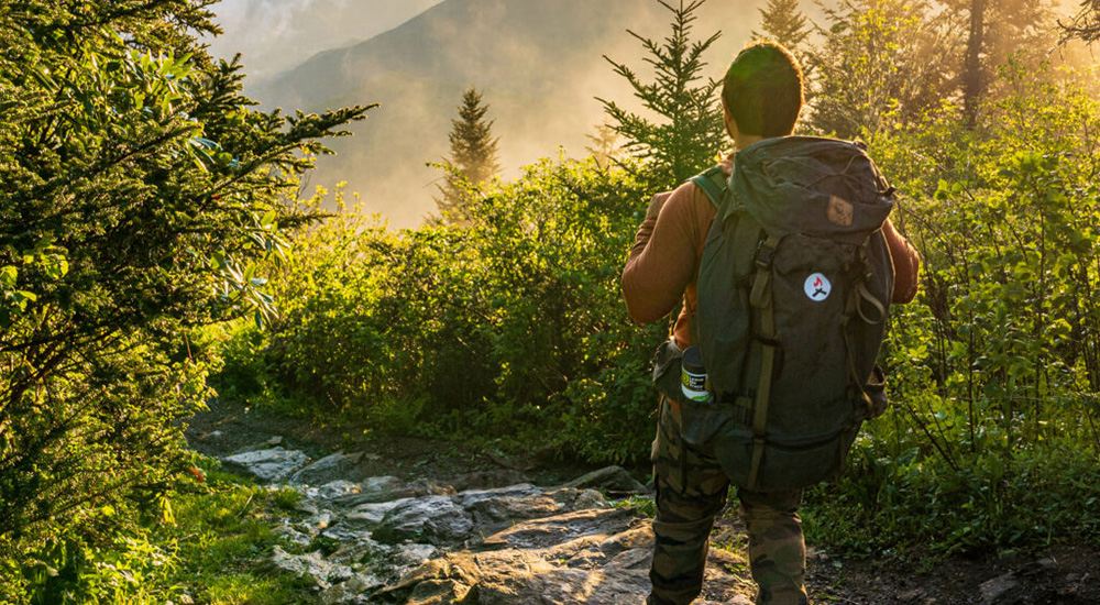 A man stands in front of a creek. The appalachian mountains can be seen in the distance
