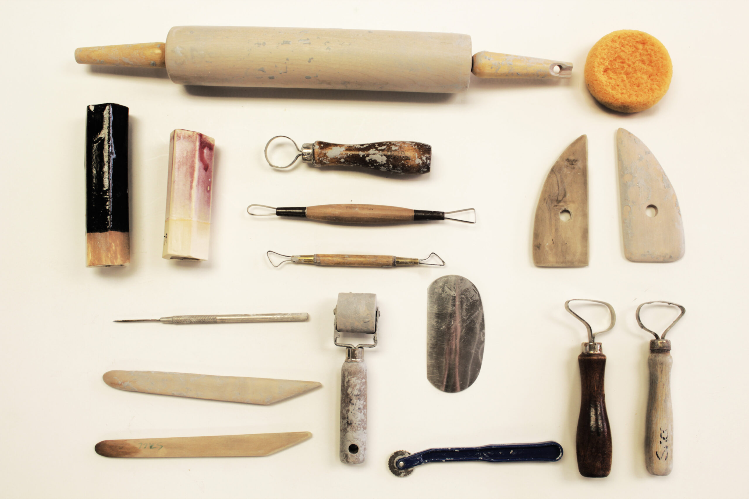 Portrait image of wheel throwing tools. You have assorted rolling pins, wood knives, sculptures, and wire loops.