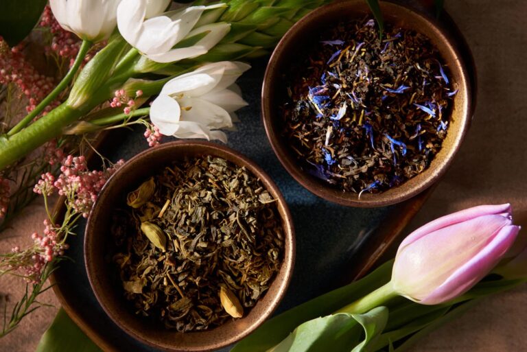Photo of two bowls of loose tea leaves with white tulips to the left of the bowls and a pink tulip to the right of the bowls