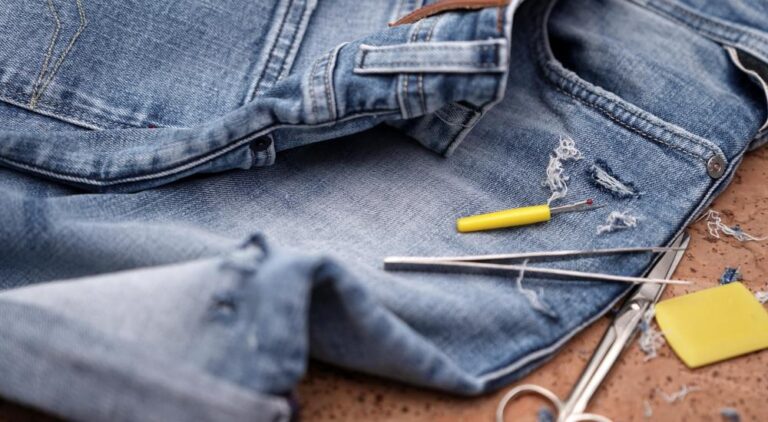 A pair of denim shorts on a craft table. A pair of tweezers, thread, and scissors rest next to the denim