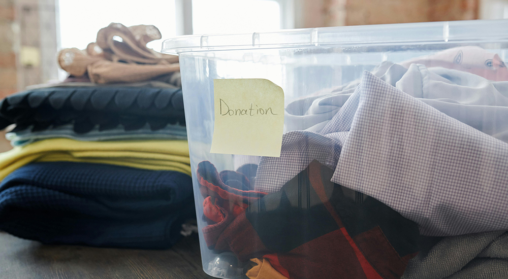 Two piles of scarves and other winter coverings. One pile are in a clear storage container and are labeled "donations"