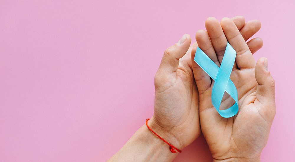 Pink banner image with a pair of upturned hands to the right of the photo. The left hand lays on the top of the right hand. The left hand has a thin red bracelet, the right hand is holding a light blue bow