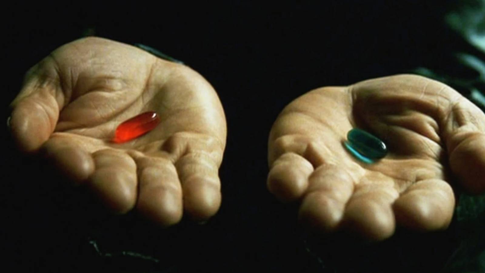 A close-up shot of two open palms extended against a dark, shadowed background. In the palm of the left hand rests a single, small red capsule pill. In the palm of the right hand rests a single, small blue capsule pill.