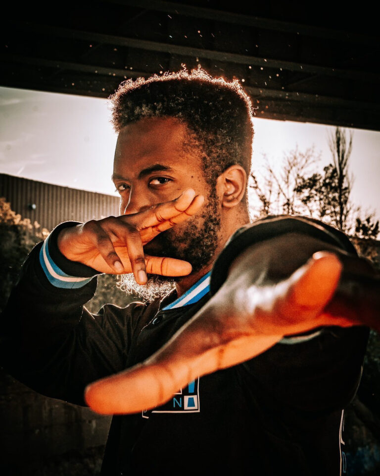 A portrait of a man extending his hand toward the camera under warm outdoor lighting.
