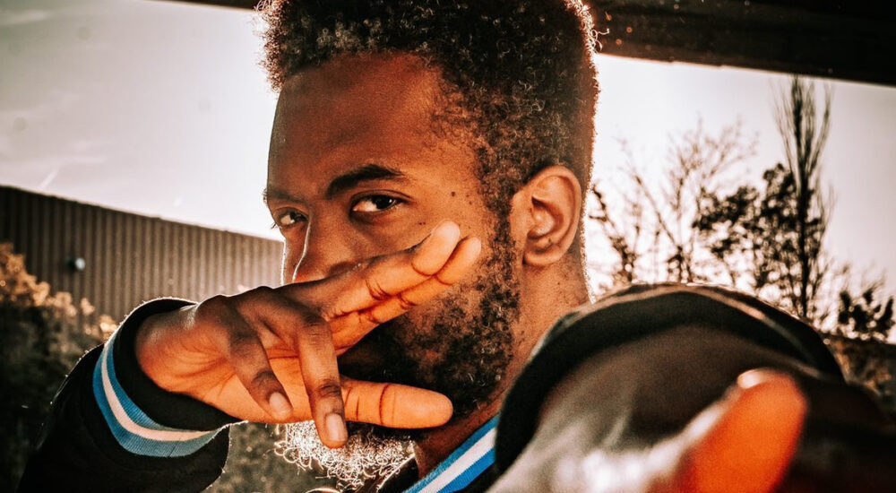 A portrait of a man extending his hand toward the camera under warm outdoor lighting.