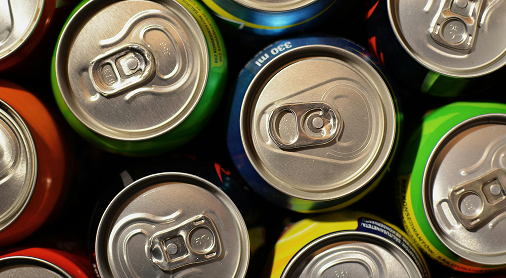 An overhead, close-up shot of several aluminum soda cans packed closely together, showing their pull-tab tops from above.