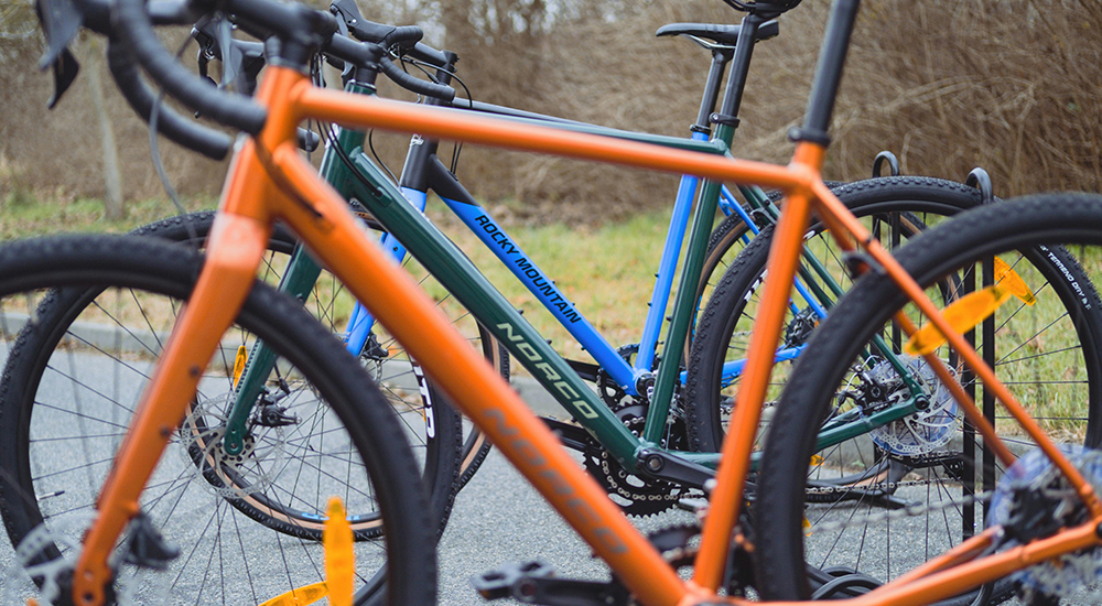 A close-up side view of a bright orange bicycle frame parked outdoors next to other bicycles.