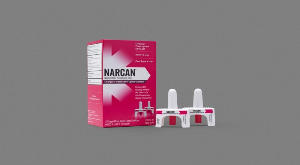 A box of Narcan nasal spray next to two single-dose nasal spray devices against a plain grey background.