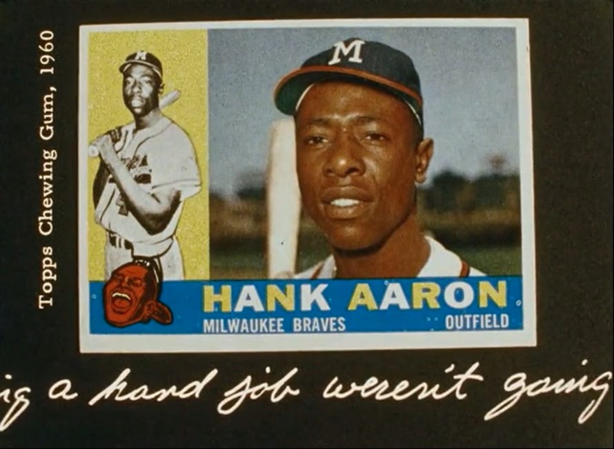 A vintage 1960 Topps Hank Aaron Milwaukee Braves baseball card displayed against a dark background, with white handwritten cursive text visible beneath the card reading, "...is a hard job weren't going".