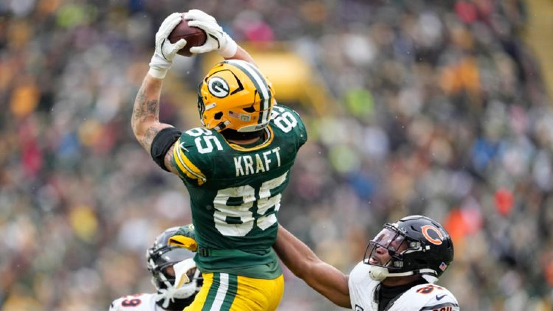 Green Bay Packers tight end Tucker Kraft (#85) reaching up to catch a football during a game, viewed from behind.