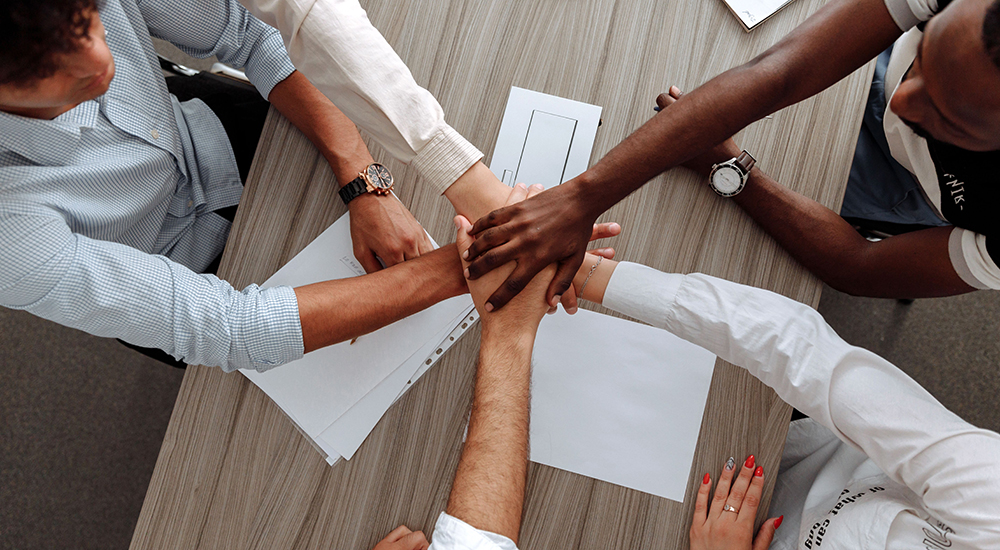 Group Collaboration with each member putting their hands together in a sign of accomplishment.