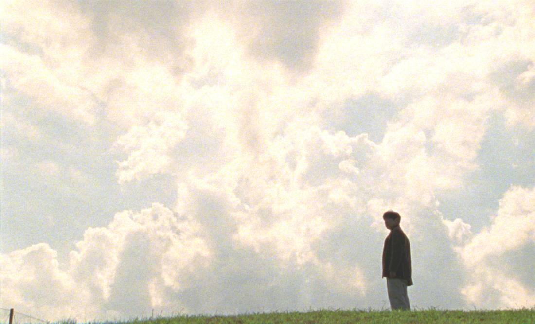 Still from the film Tony Takitani showing a solitary figure standing in a field against a vast, cloudy sky.
