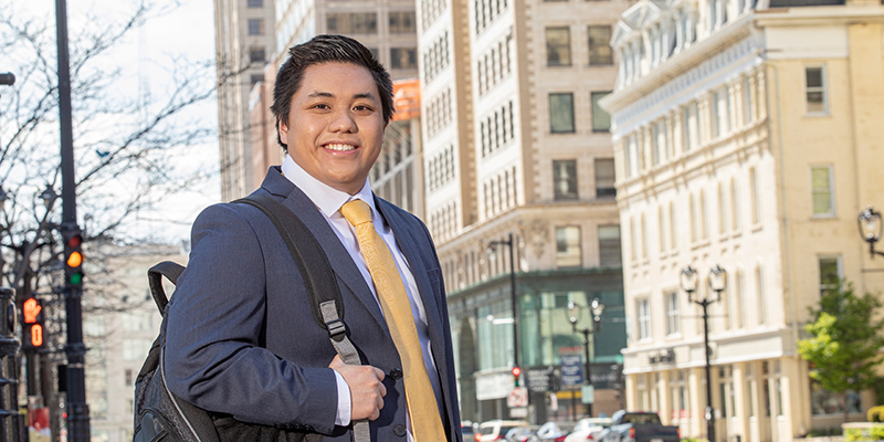 Business student (asian man) standing amongst the buildings in downtown Milwaukee