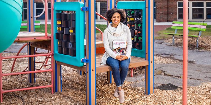 Education student (black woman) sitting on the playground at the Children's Learning Center