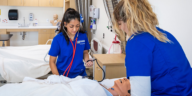 Two nursing students working on a mannequin in the simulation center on campus
