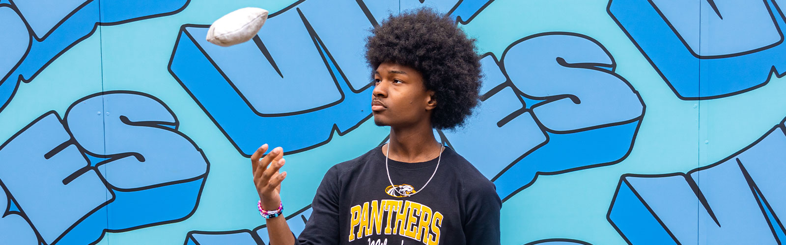 Student playing with a bag toss in front of mural