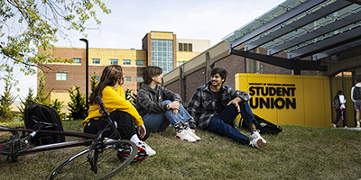 A group of four students sit on the lawn in front of the UWM Student Union.