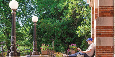 A student sits outside on he steps of Mitchell Hall on a sunny day.