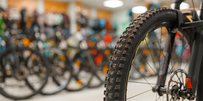 Blurred background of a row of bikes in a bike shop with a rear bike wheel in the forefront.
