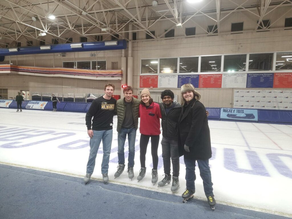 5 people standing in the middle of the Petit Center ice rink during open skate wearing winter clothes and ice skates