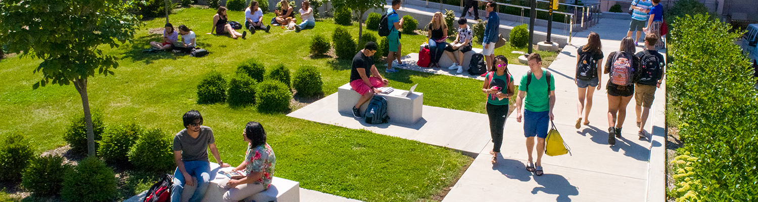 UWM students sitting and walking outside on a sunny day on campus next to the UWM Bridge near Lubar.