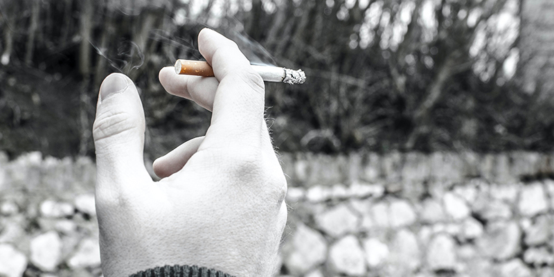 A black and white photo of a hand holding a burning cigarette