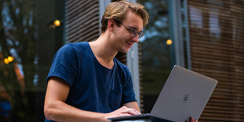 A photo of a man with glasses looking at his laptop on his lap