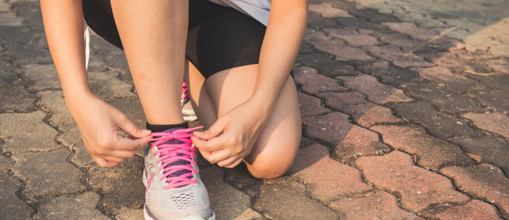 A person on a knee tightens the laces on a running shoe