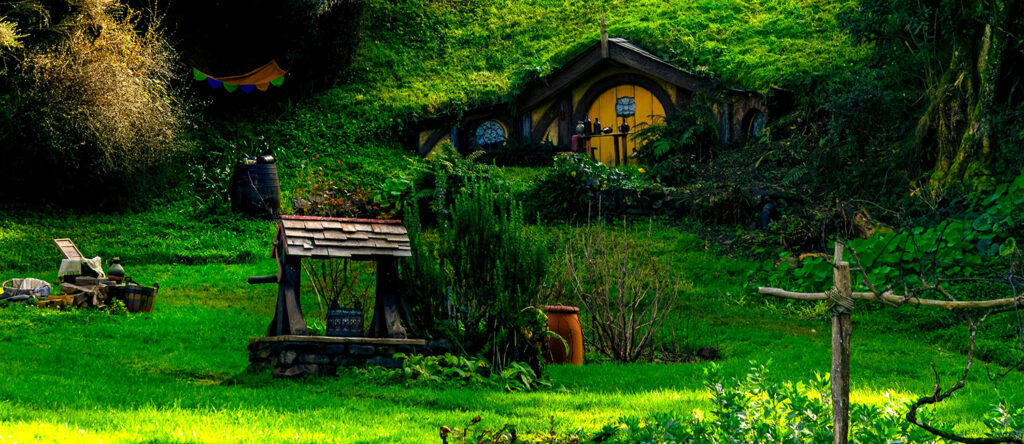 A lush green hillside with a well and a small hut in the background