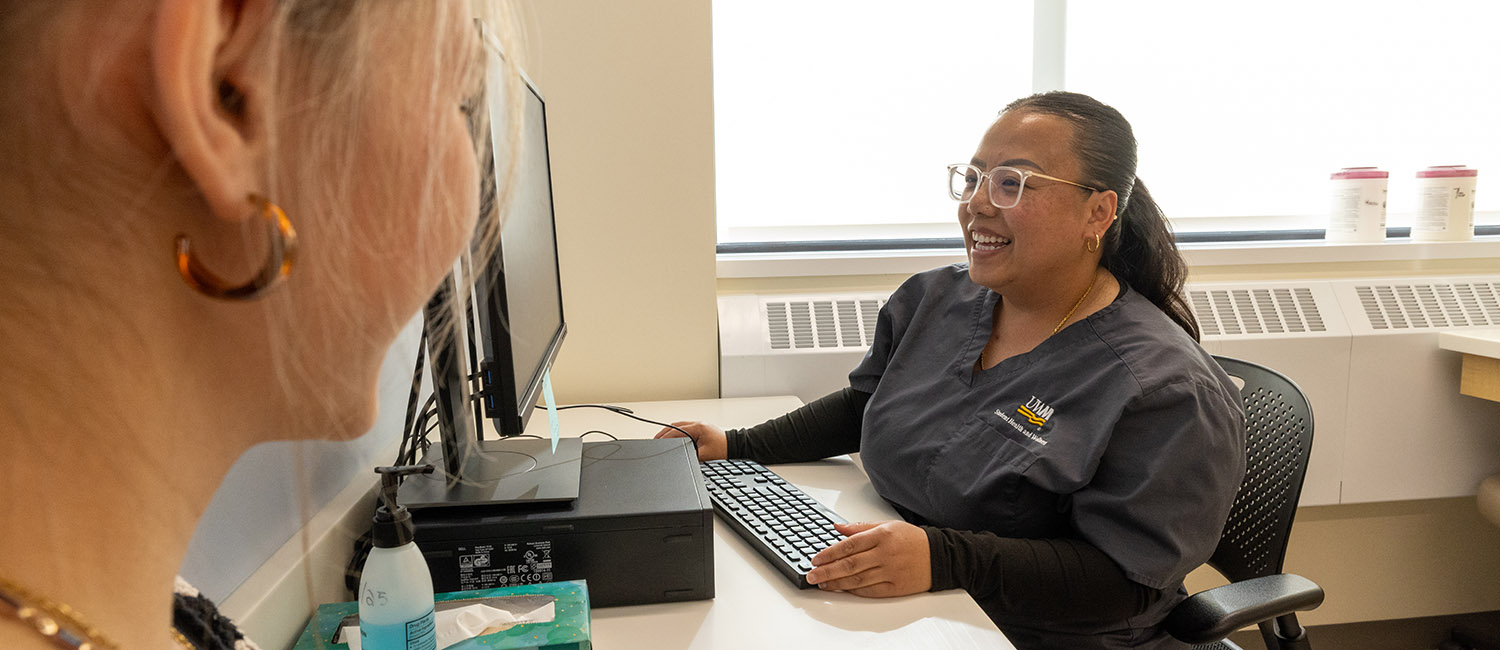 A nurse sitting at a computer smiles while talking to a patient at the Student Health and Wellness Center