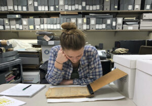 Girl leaning over old document in room filled with archival materials