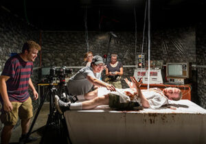 Horror movie set with actor on table and tech crew surrounding