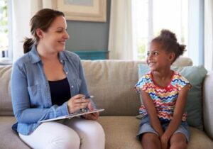 Young woman sitting on couch with clipboard talking to little girl