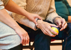 Elderly person holding a ball while aide holds their wrist