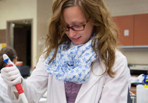 Girl wearing lab coat and scarf while using pipette in a lab