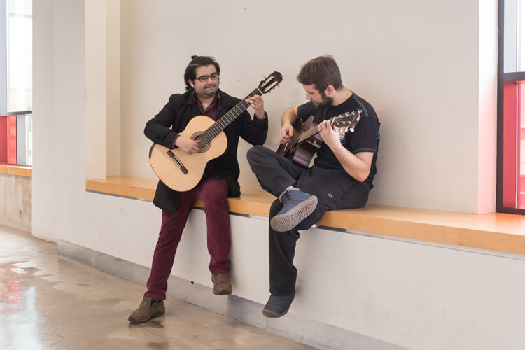 Two students playing guitar in the hallway.