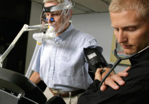 Person with stethoscope measuring heartbeat of man on treadmill wearing oxygen mask