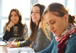 Three female students sitting in class in front of windows