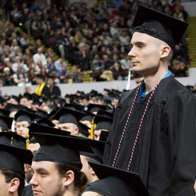 Student standing up at graduation ceremony wearing graduation garb