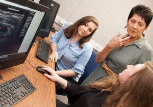Two female students at computers talking to female instructor