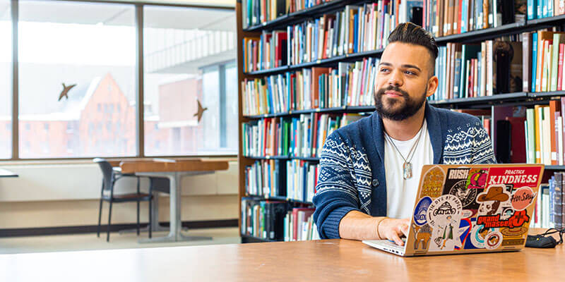 student sitting in library in front of laptop looking to the right