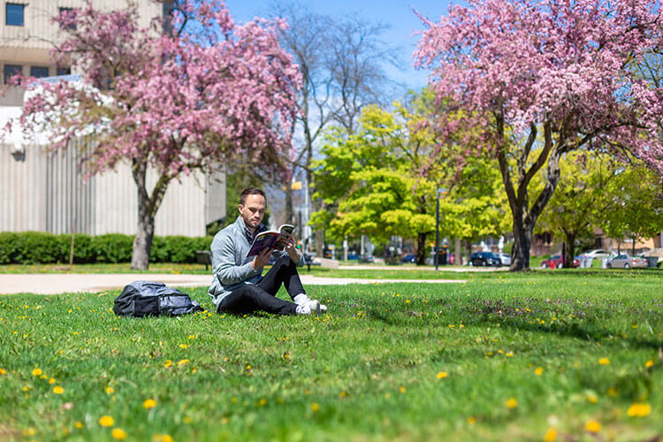 Male student sitting in grass in spring reading a book