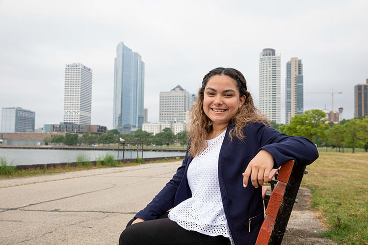 Female student sitting on bench with Milwaukee downtown skyline behind her