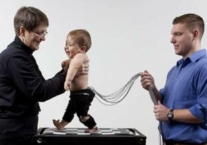 Two researchers holding a baby with electrodes attached while walking on a treadmill