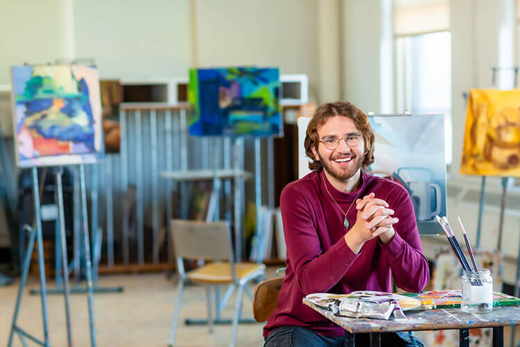 Art education major sitting at table in front of paintings