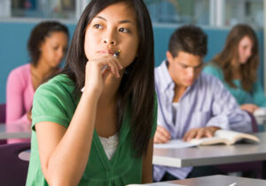 Female Asian-American student sitting in class and thinking while holding a pen