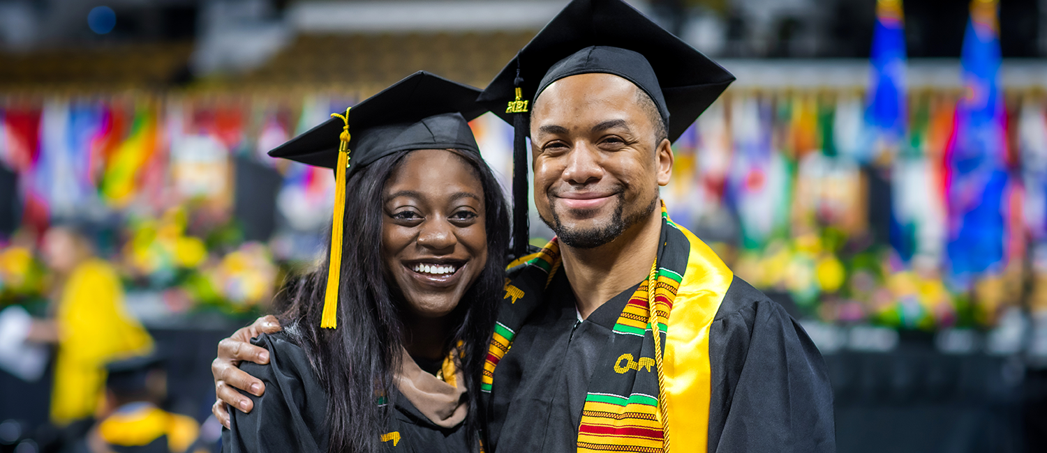 Two graduating UWM students in their cap and gown smiling at the camera