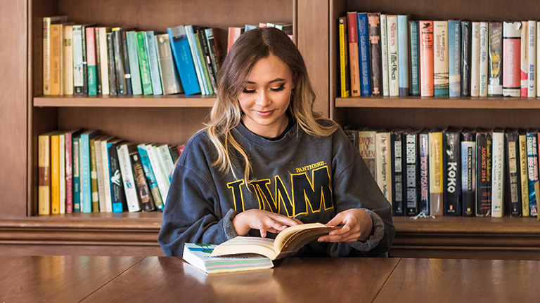 UWM student in library reading a book