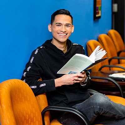 UWM student Jesus sitting in chair with open book and smiling